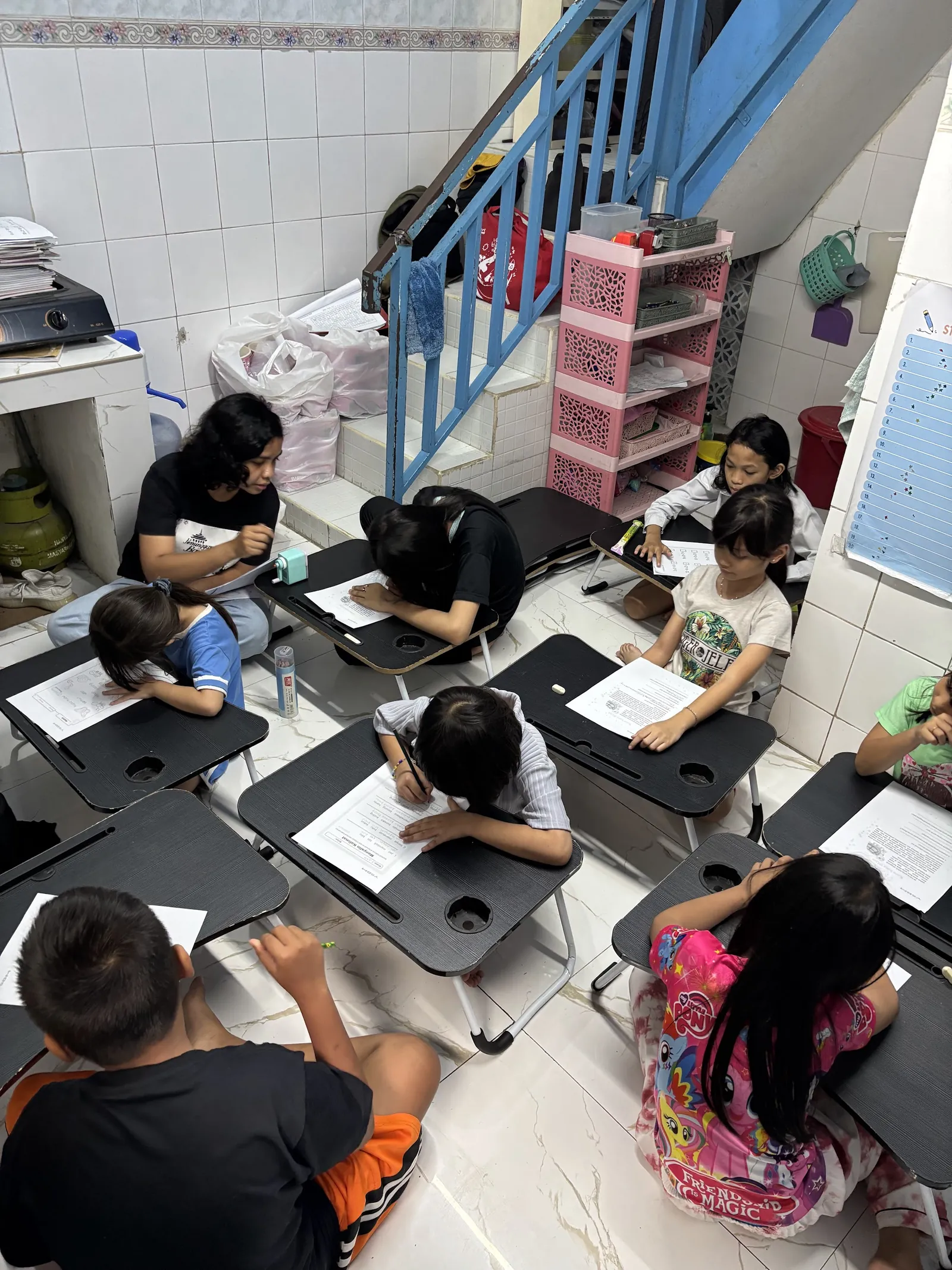 Children complete worksheets at small desks in the YSBM learning house