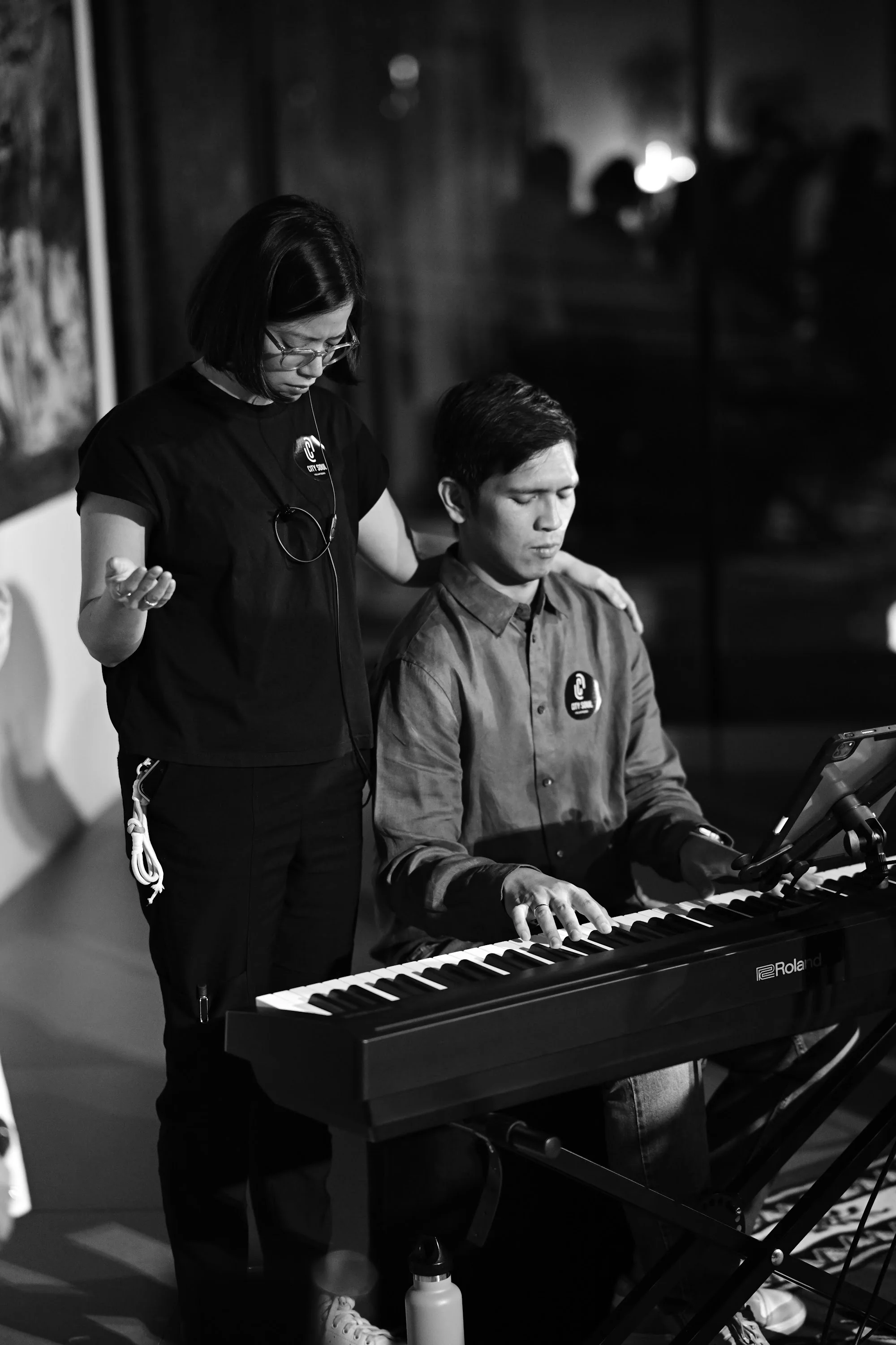 A keyboard player worships while another participant rests a hand on his shoulder